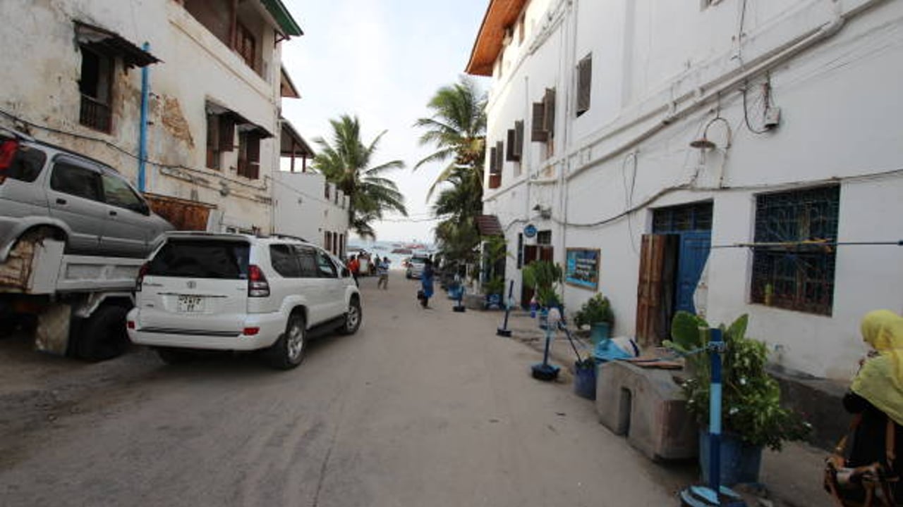 A white Toyota Land Cruiser Prado parked on a sandy side street in Stone Town