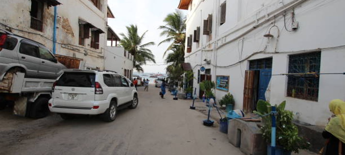 A white Toyota Land Cruiser Prado parked on a sandy side street in Stone Town