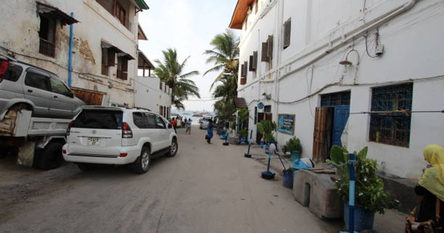 A white Toyota Land Cruiser Prado parked on a sandy side street in Stone Town
